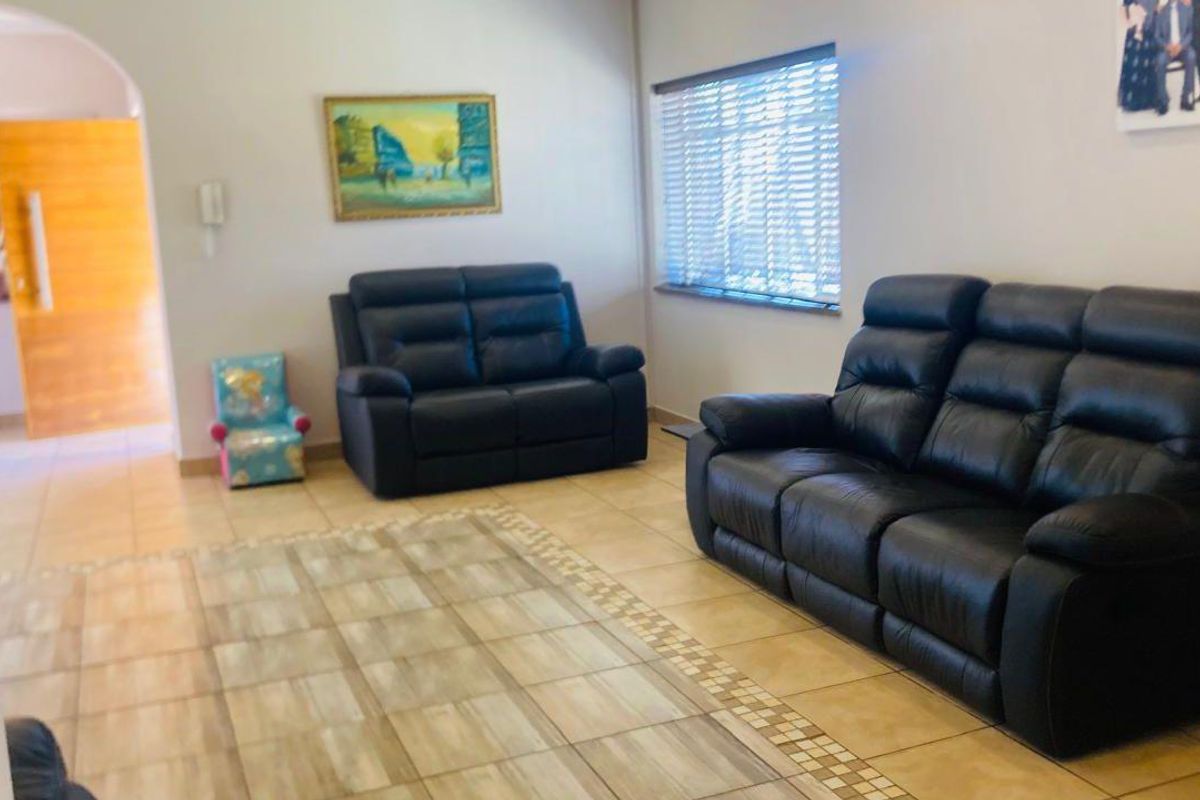 A living room featuring tiled flooring, an arched entryway, and venetian blinds, providing a functional and neutral space for relaxation.