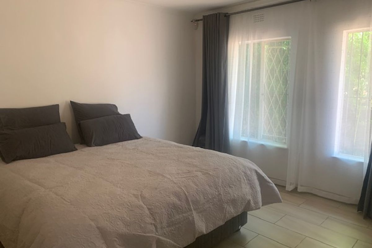 A bright bedroom featuring tiled flooring, large windows with security bars, and neutral wall finishes.