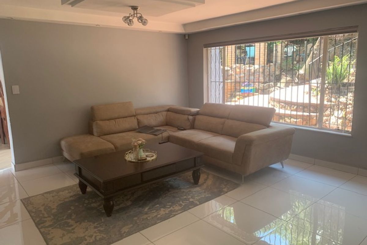 A bright living room featuring large windows with security bars, polished floor tiles, and a modern recessed ceiling design.