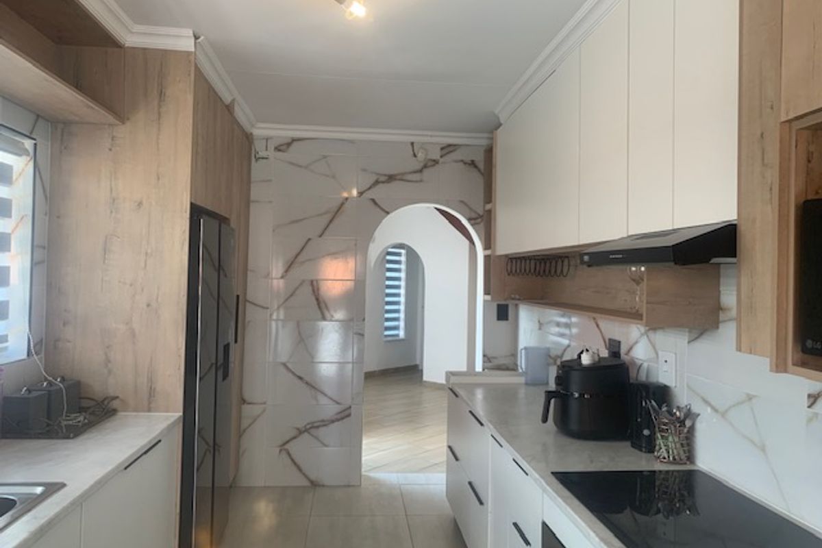 Modern kitchen featuring light wood-grain cabinetry, marble-effect tiled splashbacks, integrated hob, extractor fan, and a distinctive arched doorway leading to adjacent living spaces.