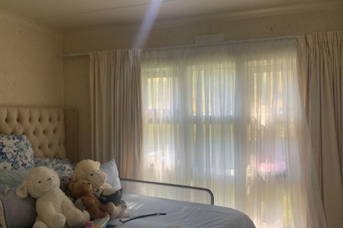 A bedroom featuring a large window with curtain tracks and built-in cupboard space, showing signs of wear on the wall surfaces.