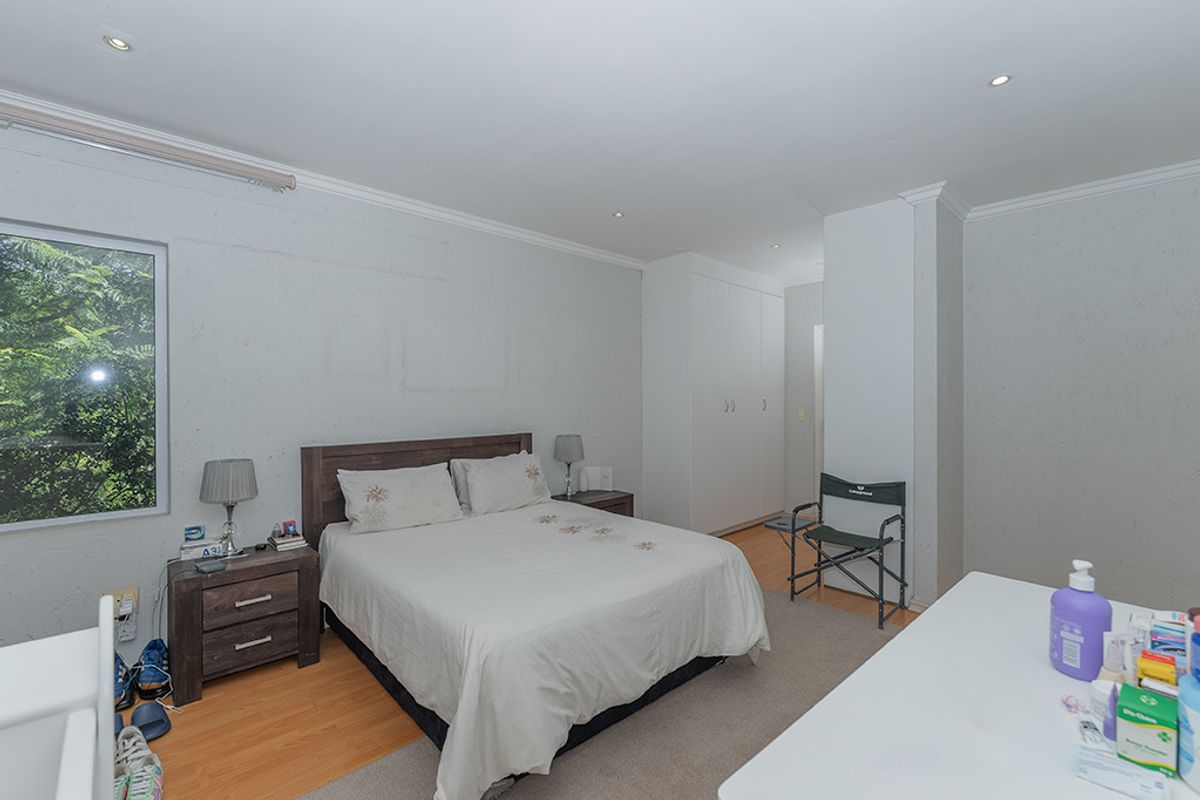 Spacious bedroom featuring built-in cupboards, recessed downlighting, and laminate flooring, offering a functional layout with potential for cosmetic updates.