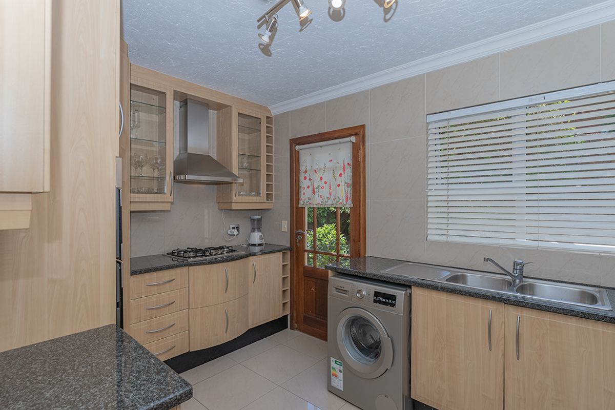 A functional kitchen featuring light-wood cabinetry, granite countertops, a gas hob, stainless steel extractor fan, and integrated laundry facilities with direct garden access.