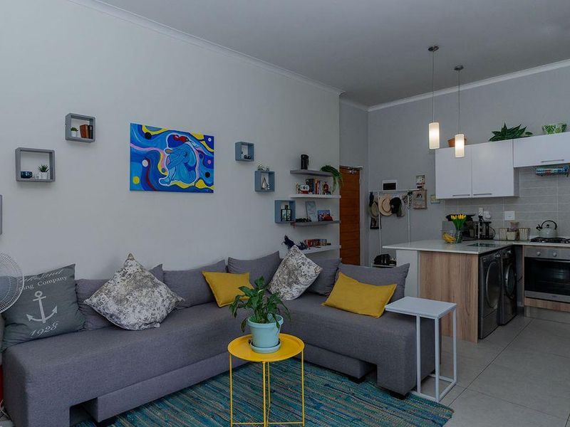 Open-plan living area featuring a modern kitchen with built-in cabinetry, oven, hob, and tiled flooring, seamlessly integrated with the lounge space.