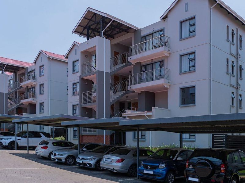 Exterior view of a modern apartment complex featuring multi-story residential blocks with balconies and dedicated covered parking bays.