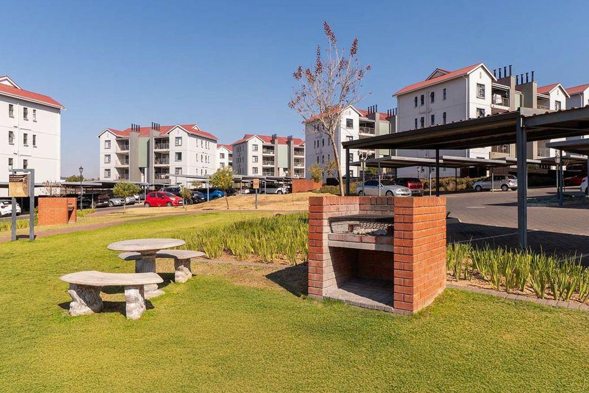 Communal outdoor area featuring a brick braai, landscaped lawn, and covered parking facilities within the apartment complex grounds.