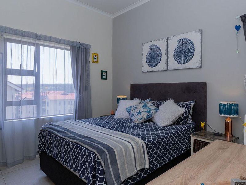 A well-maintained bedroom featuring tiled flooring, neutral wall tones, and a large window providing natural light.