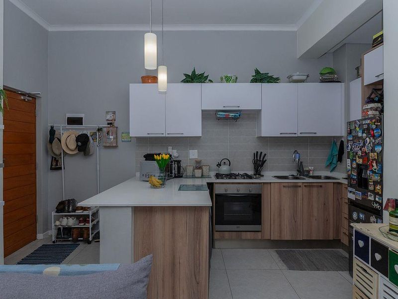 Modern kitchen featuring white upper cabinets, wood-finish lower cabinetry, stone countertops, built-in oven, gas hob, and a double sink with tiled backsplash.