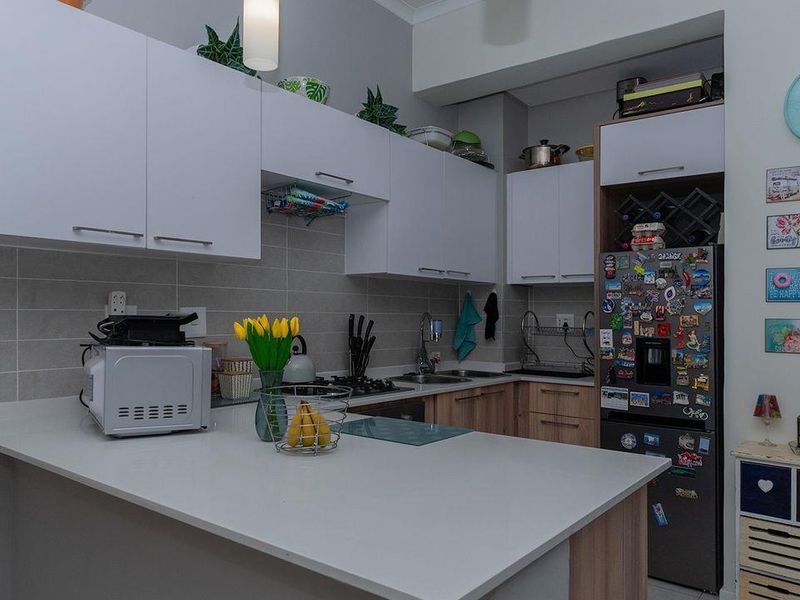 A modern kitchen featuring white upper cabinetry, wood-tone lower cabinets, stone countertops, a tiled backsplash, and integrated gas hob with extractor fan.