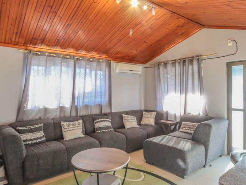 A living room featuring a vaulted timber-clad ceiling, tiled flooring, and a wall-mounted air conditioning unit, providing a comfortable and functional living space.