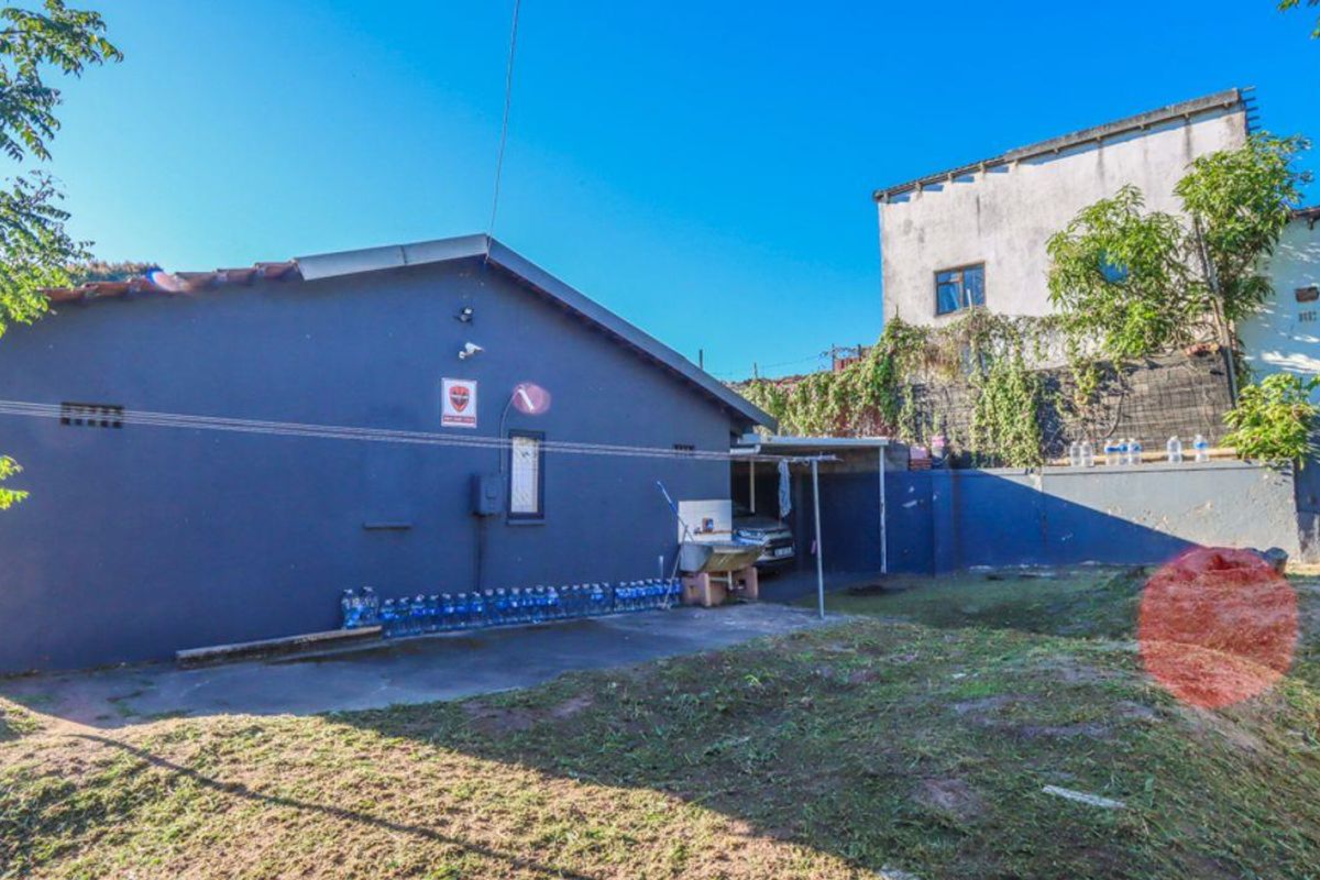 Rear exterior view of the property featuring a paved area, concrete wash basin, and retaining wall with an uneven garden space.