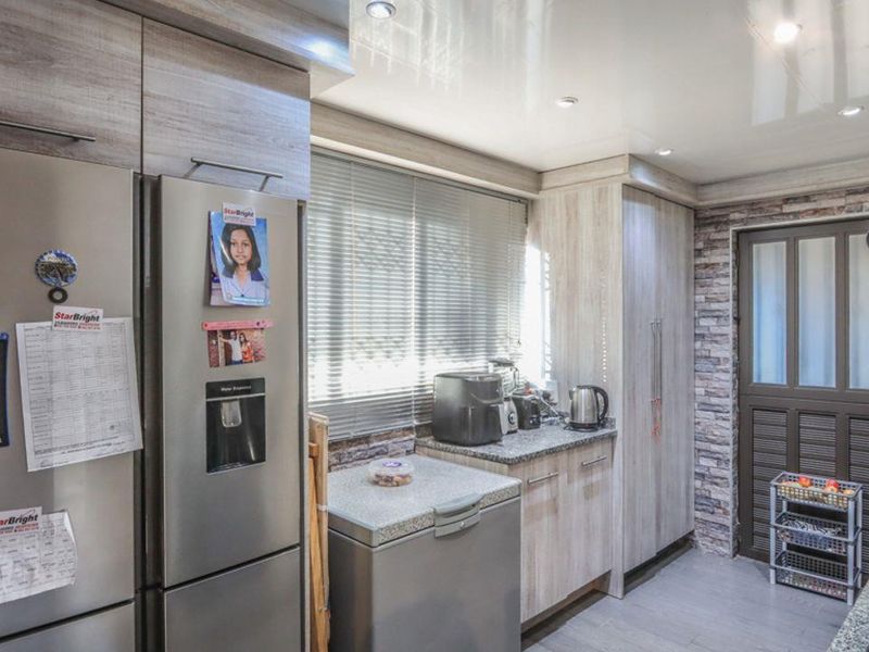 A functional kitchen featuring light wood-grain cabinetry, granite countertops, a stone-cladding feature wall, and recessed ceiling lighting.