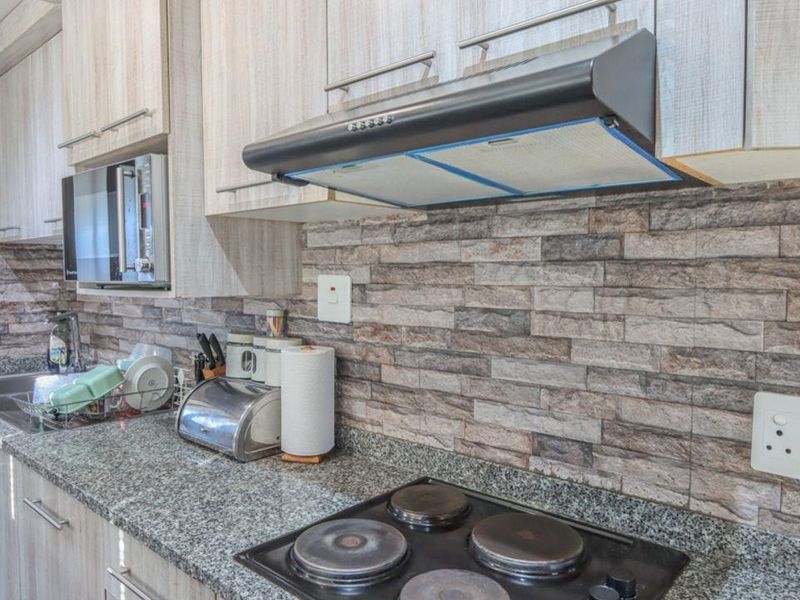 A functional kitchen featuring granite countertops, stone veneer backsplash, built-in cabinetry, and integrated appliances including an electric hob and extractor fan.