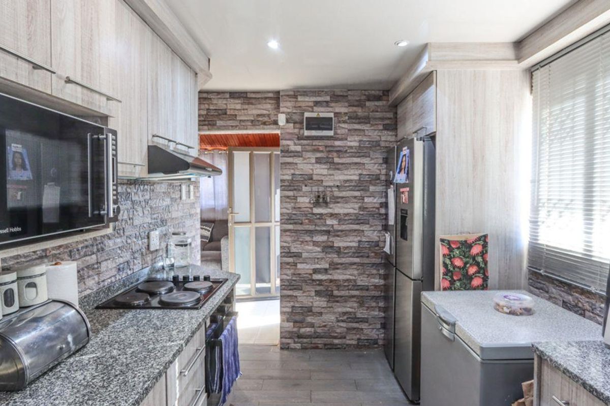 A functional kitchen featuring light wood-grain cabinetry, granite countertops, an electric hob, and a distinctive stone-clad feature wall.