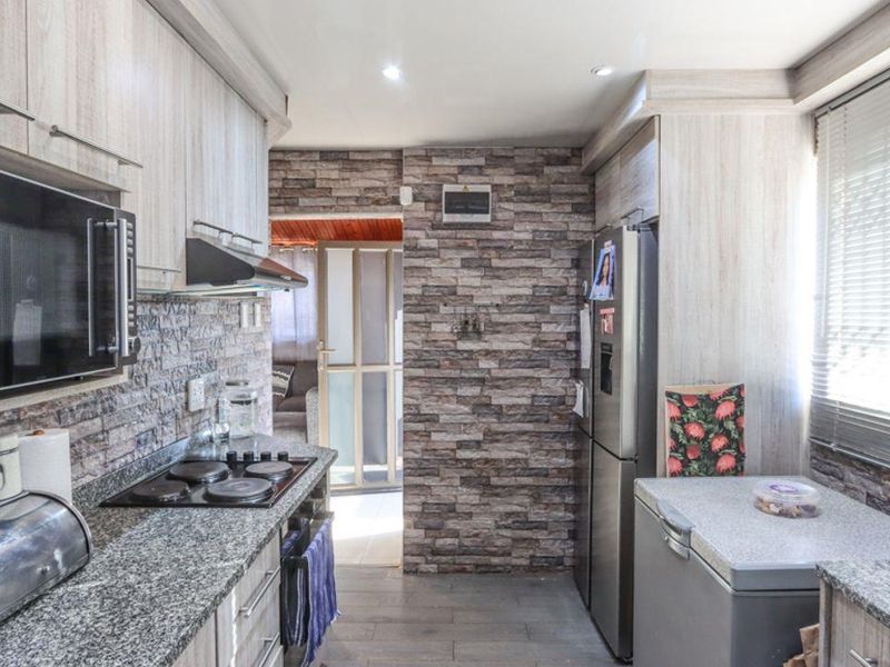 A functional kitchen featuring light wood-grain cabinetry, granite countertops, an electric hob, and a distinctive stone-clad feature wall.