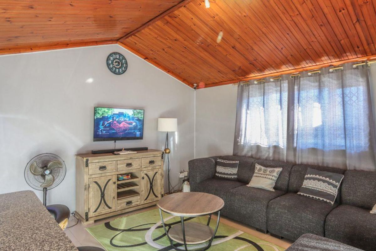 A living room featuring a distinctive timber-clad raked ceiling, tiled flooring, and a wall-mounted split-system air conditioner.