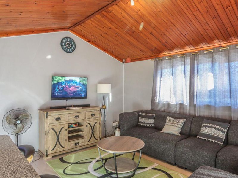 A living room featuring a distinctive timber-clad raked ceiling, tiled flooring, and a wall-mounted split-system air conditioner.