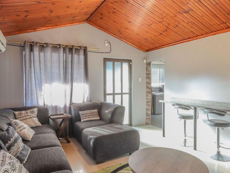 Open-plan living area featuring a vaulted timber-clad ceiling, tiled flooring, split-system air conditioning, and a built-in granite breakfast bar.