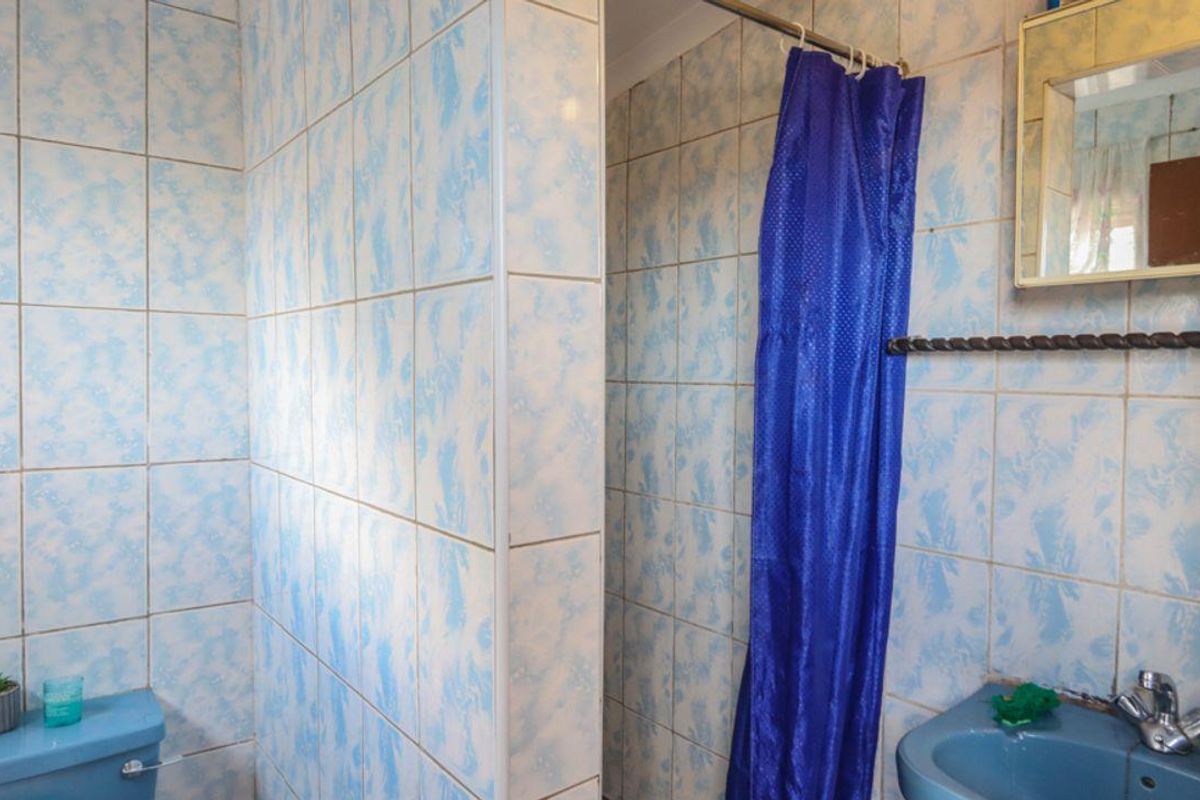 A dated bathroom featuring blue sanitary ware, patterned wall tiles, and a shower area with a curtain.