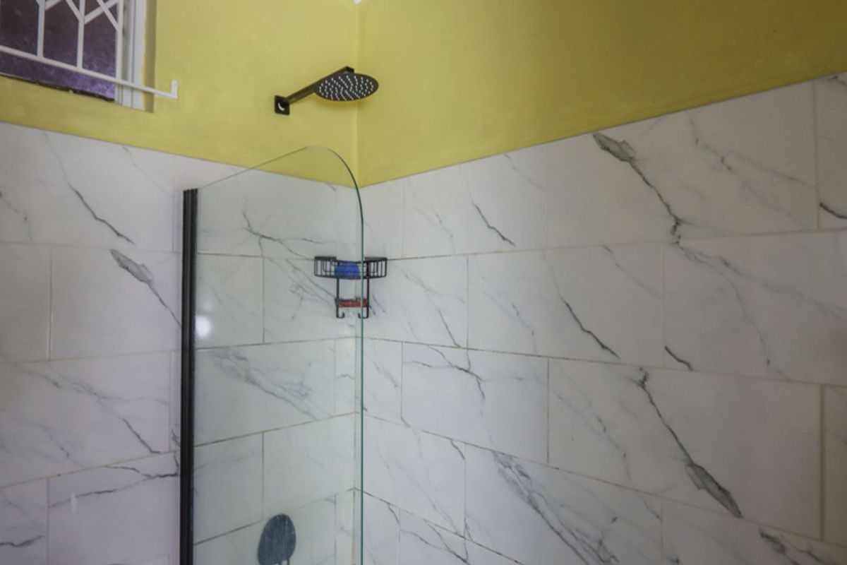 A modern shower enclosure featuring marble-look wall tiles, a sleek black rainfall showerhead, and a glass partition.