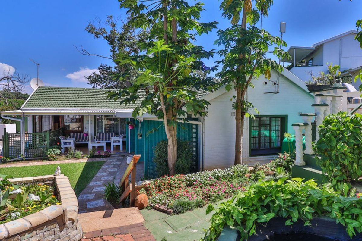 A charming residential exterior featuring a covered patio, landscaped garden, and established trees, offering a pleasant outdoor living space.