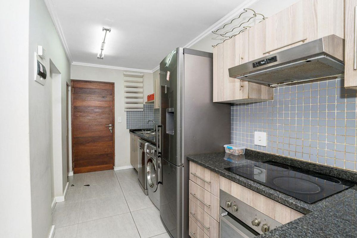 Compact kitchen featuring granite countertops, built-in oven, electric hob, extractor fan, tiled backsplash, and light wood cabinetry with integrated laundry appliance space.
