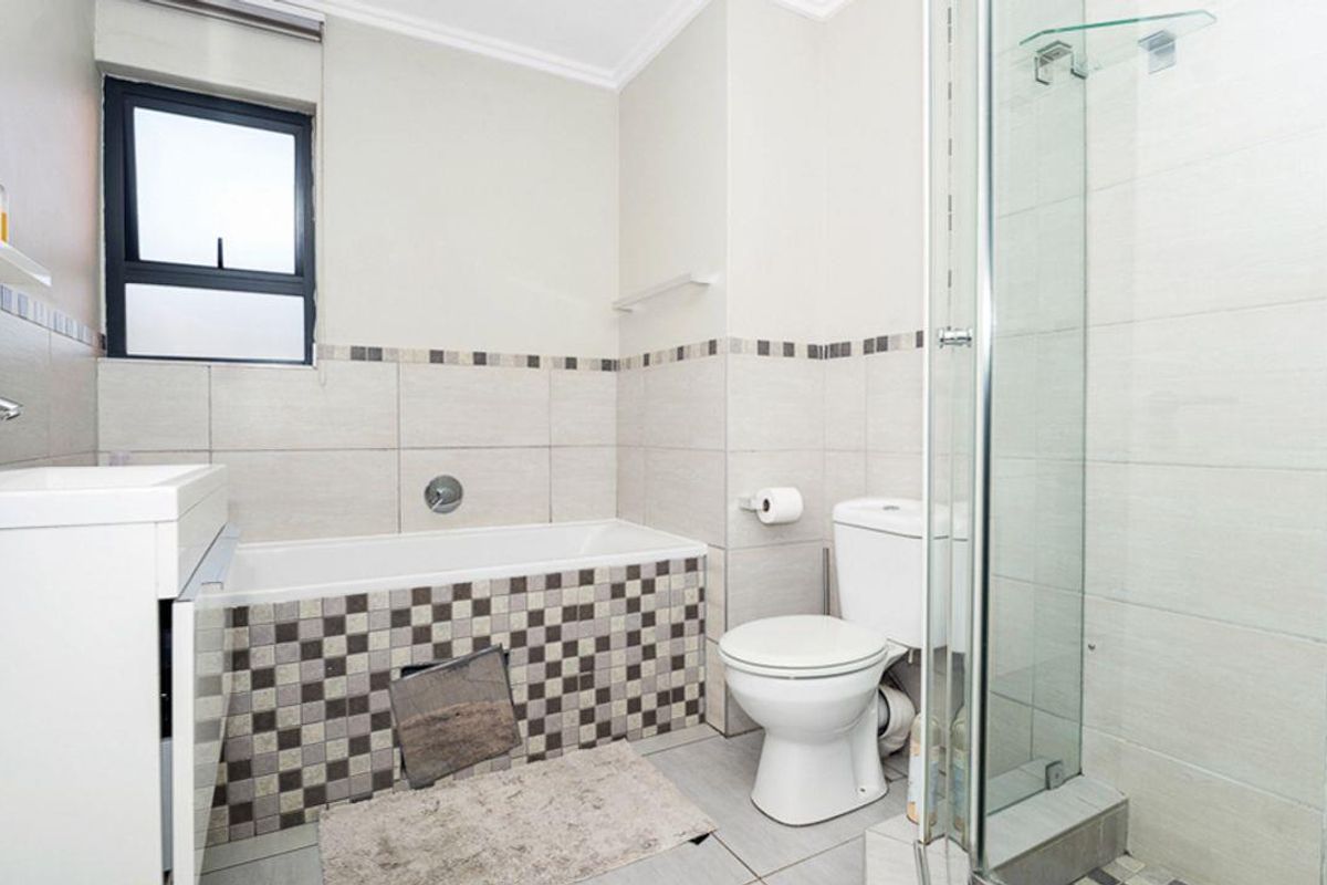 A functional bathroom featuring a built-in bathtub with mosaic tile detailing, a separate glass-enclosed shower, and a standard toilet.