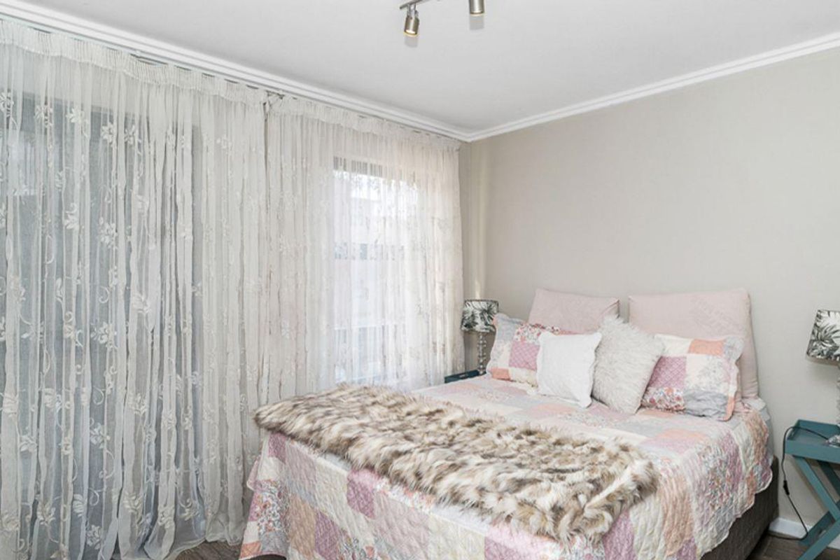 A well-lit bedroom featuring neutral wall tones, crown molding, and a large sliding glass door with floor-to-ceiling sheer curtains.