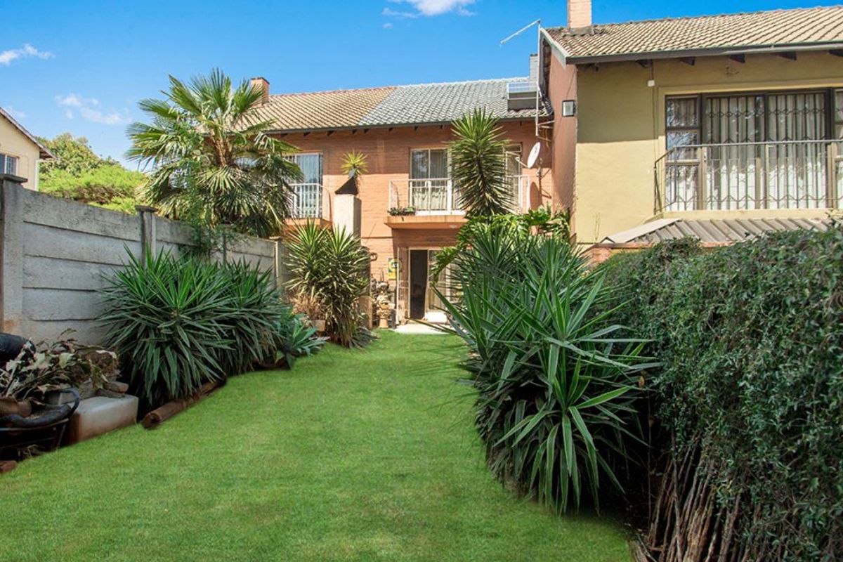 A private rear garden featuring a well-maintained lawn, established landscaping, and a brick townhouse facade with upper-level balconies.
