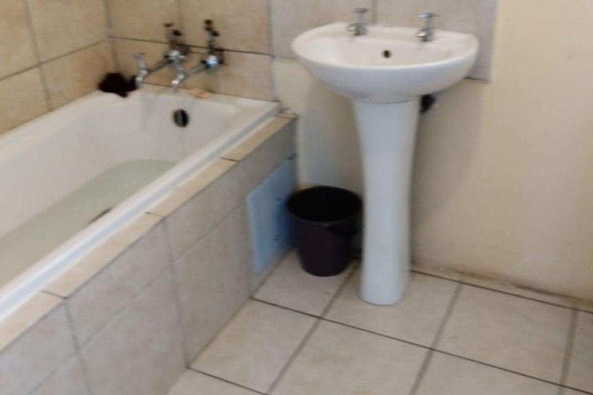 A functional bathroom featuring a standard bathtub, pedestal basin, and toilet with tiled flooring and wall surrounds.