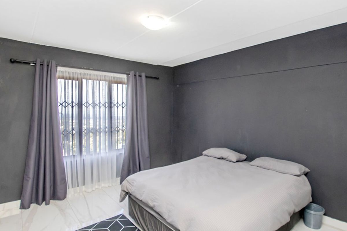 A bedroom featuring dark-toned walls, tiled flooring, and a window fitted with security bars and curtains.