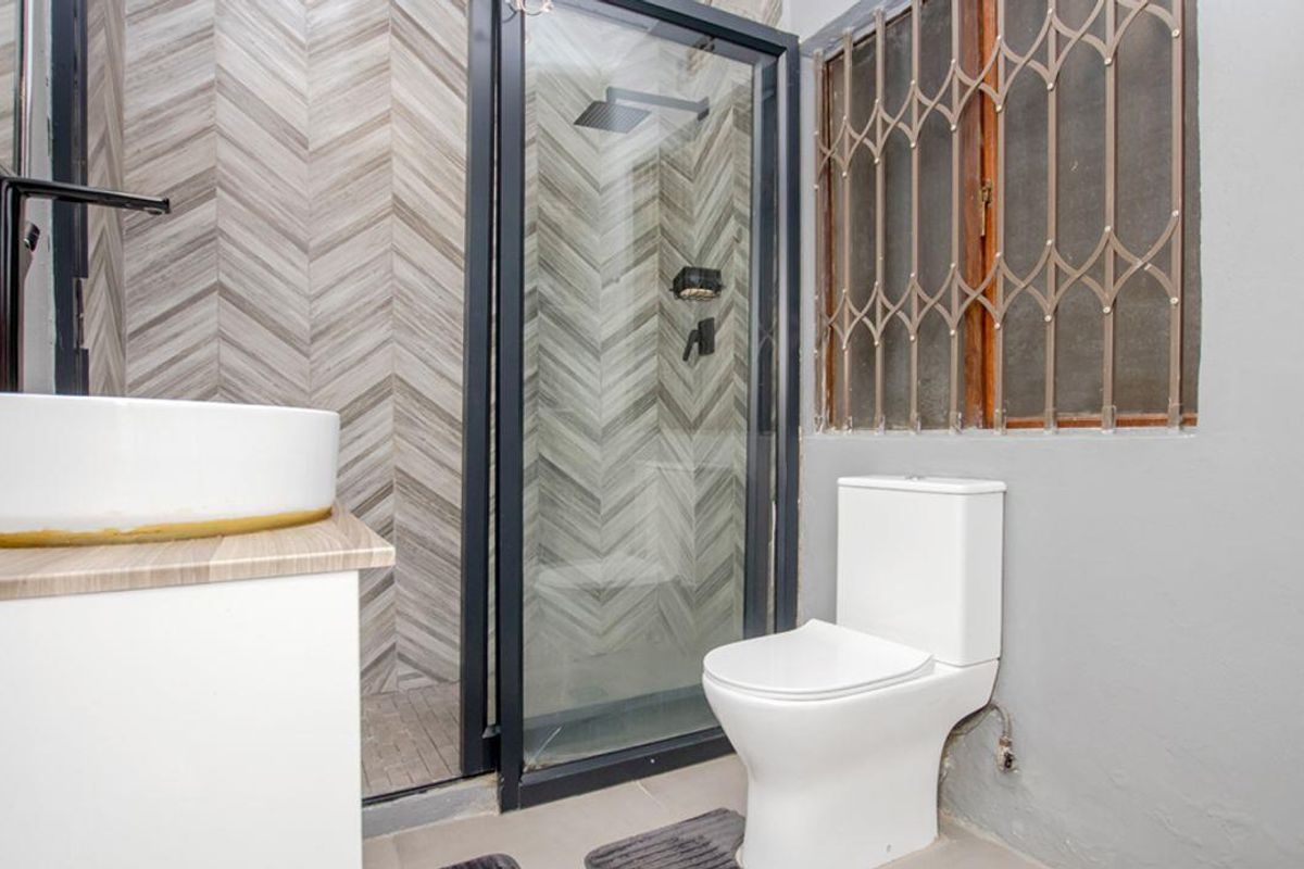 Modern bathroom featuring a glass-enclosed shower with chevron-patterned wall tiles, a contemporary vessel sink vanity, and a white toilet.