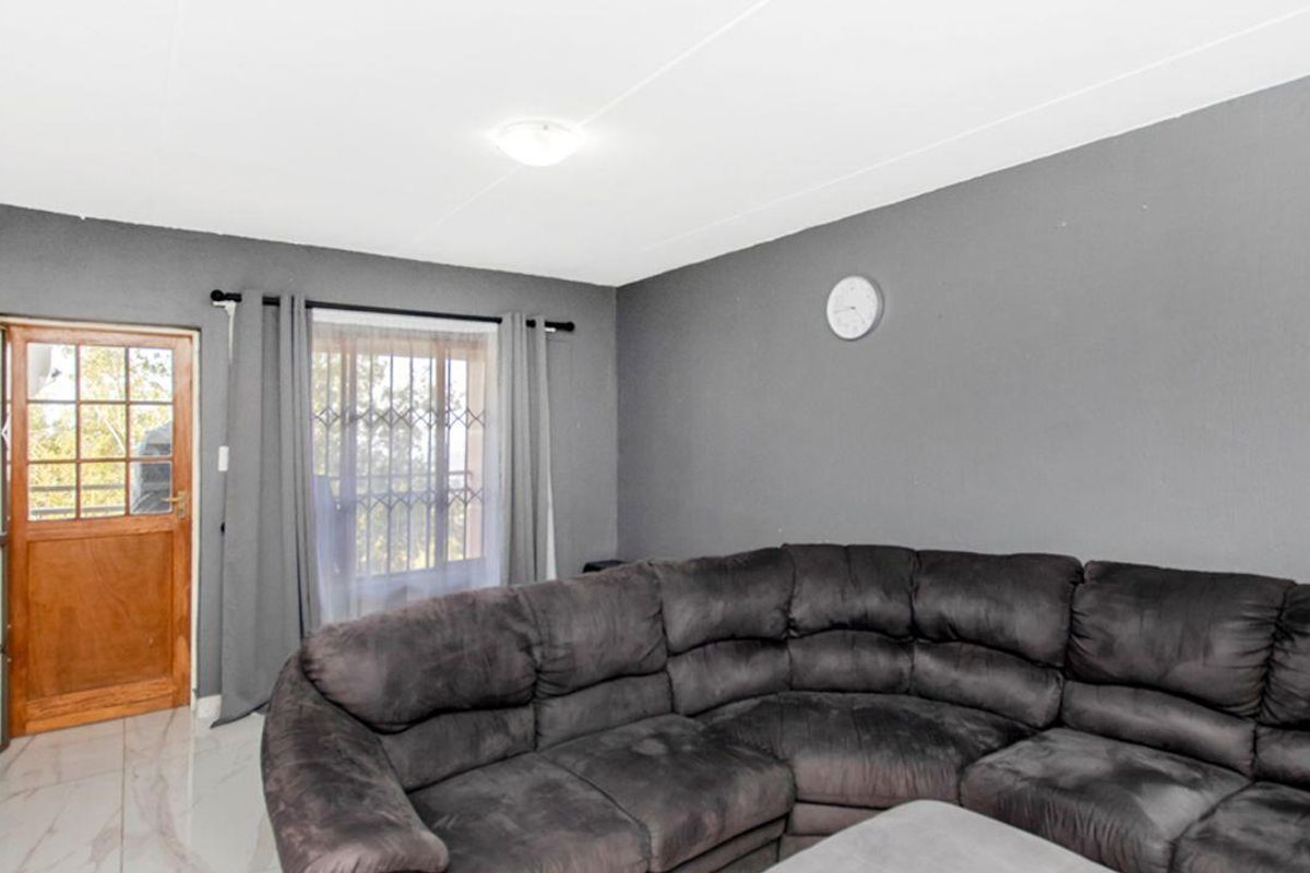 A living room featuring tiled flooring, grey painted walls, and a security gate leading to an outdoor area.