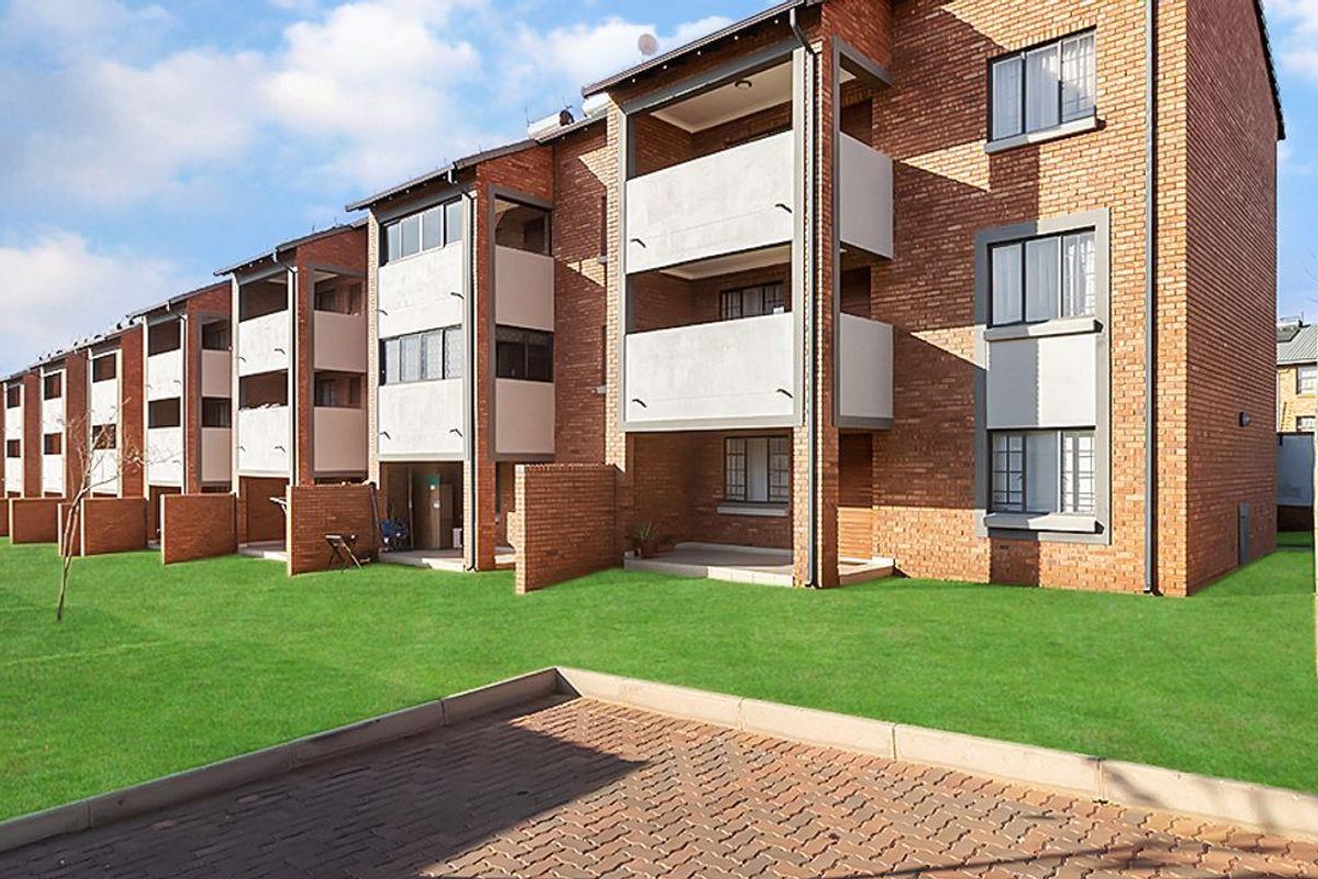 Exterior view of a multi-story apartment complex featuring face-brick facades, private balconies, and a well-maintained communal lawn area.