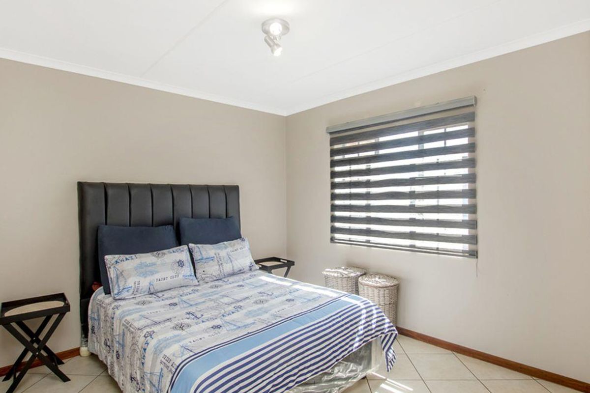 A well-maintained bedroom featuring neutral wall tones, tiled flooring, a built-in wardrobe, and a modern roller blind.