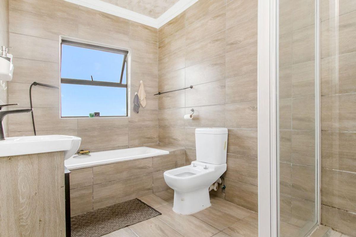 Modern bathroom featuring floor-to-ceiling neutral tiling, a built-in bathtub, a separate glass-enclosed shower, and a contemporary vanity unit.