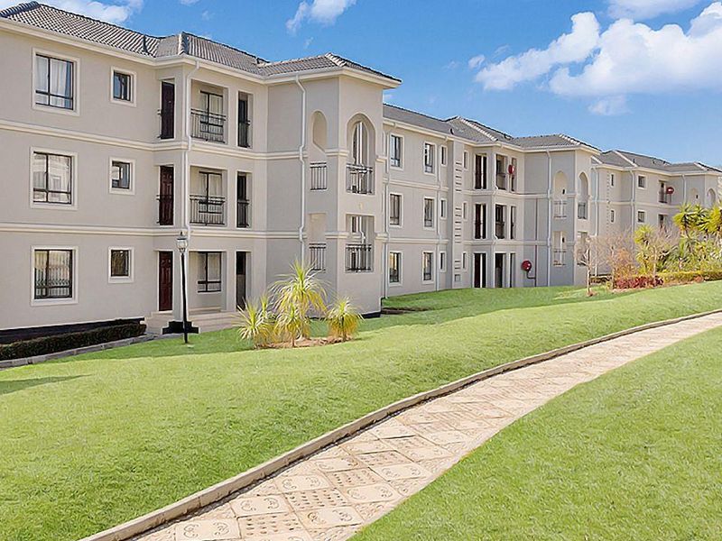 A view of the apartment complex exterior featuring multi-story residential blocks with balconies, paved walkways, and well-maintained landscaped garden areas.