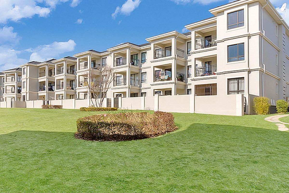 A view of the apartment complex exterior featuring multi-story residential units with private balconies and well-maintained communal garden areas.