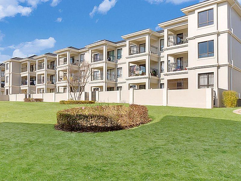 A view of the apartment complex exterior featuring multi-story residential units with private balconies and well-maintained communal garden areas.