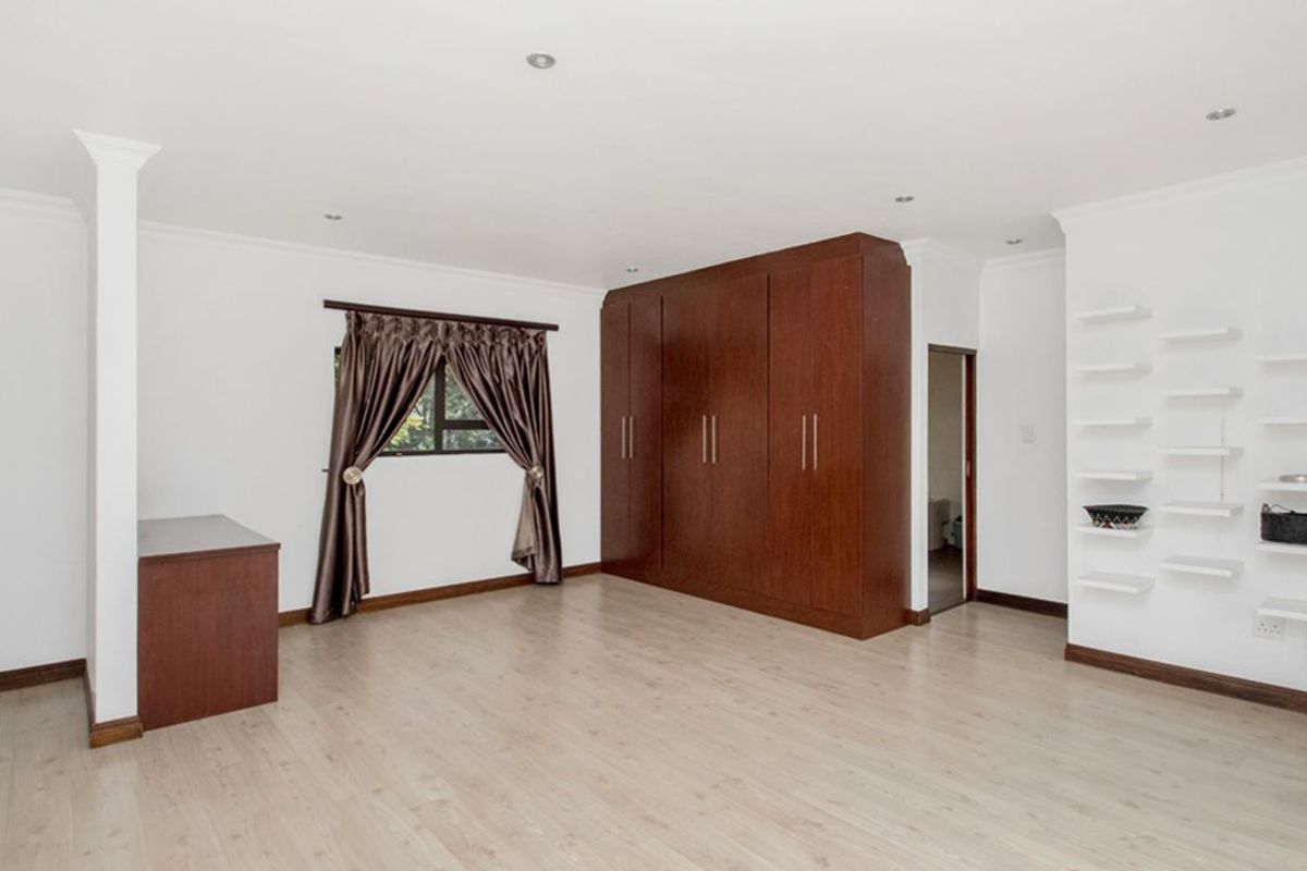 Spacious bedroom featuring light wood-look flooring, recessed ceiling lighting, and extensive built-in dark wood cabinetry for ample storage.