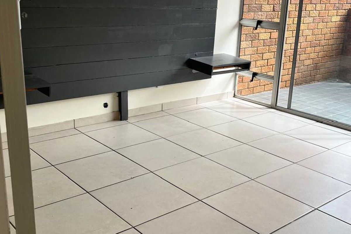 A bright living area featuring large glass sliding doors, tiled flooring, and a built-in black feature wall panel with floating shelves.