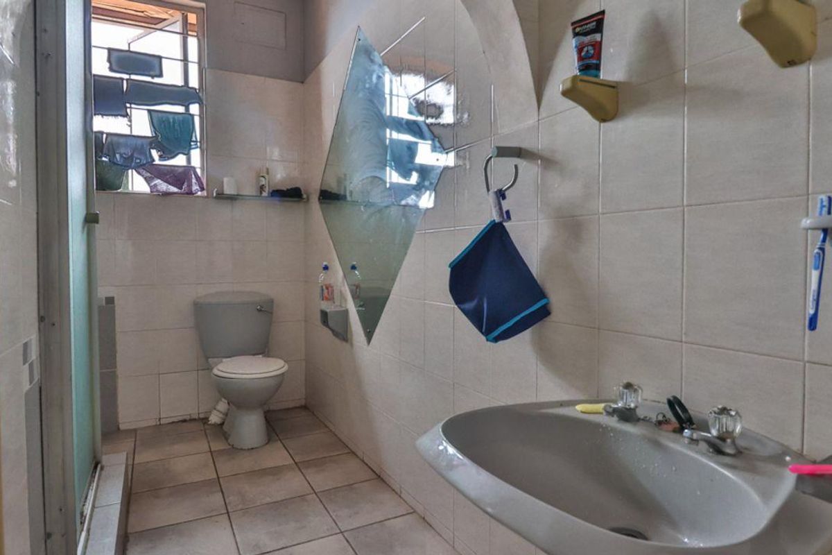 A functional bathroom featuring tiled walls, a pedestal basin, and a standard toilet, requiring cosmetic updates to modernize the space.