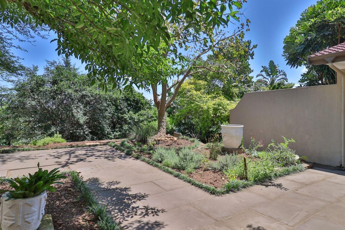 A well-maintained rear garden area featuring paved pathways, established trees, and landscaped garden beds adjacent to the townhouse structure.