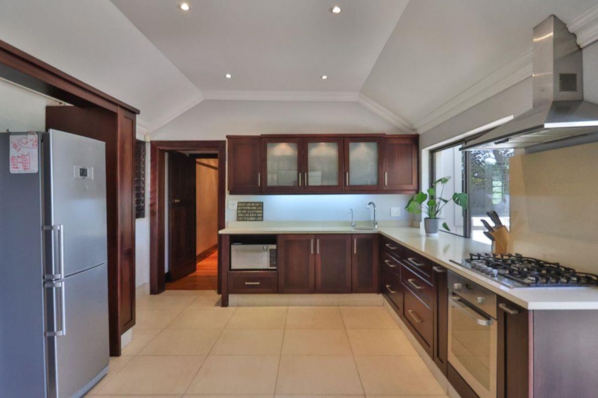 A well-appointed kitchen featuring dark wood cabinetry, stone countertops, a built-in oven, gas hob, stainless steel extractor fan, and recessed ceiling lighting.