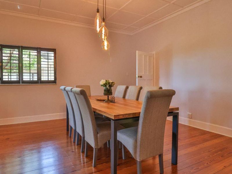 A bright dining room featuring polished timber flooring, decorative ceiling panels, and dark-framed window shutters.
