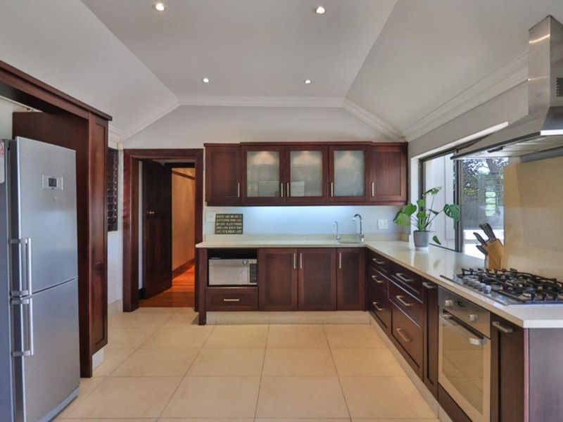 A well-appointed kitchen featuring dark wood cabinetry, stone countertops, a built-in oven, gas hob, stainless steel extractor fan, and recessed ceiling lighting.