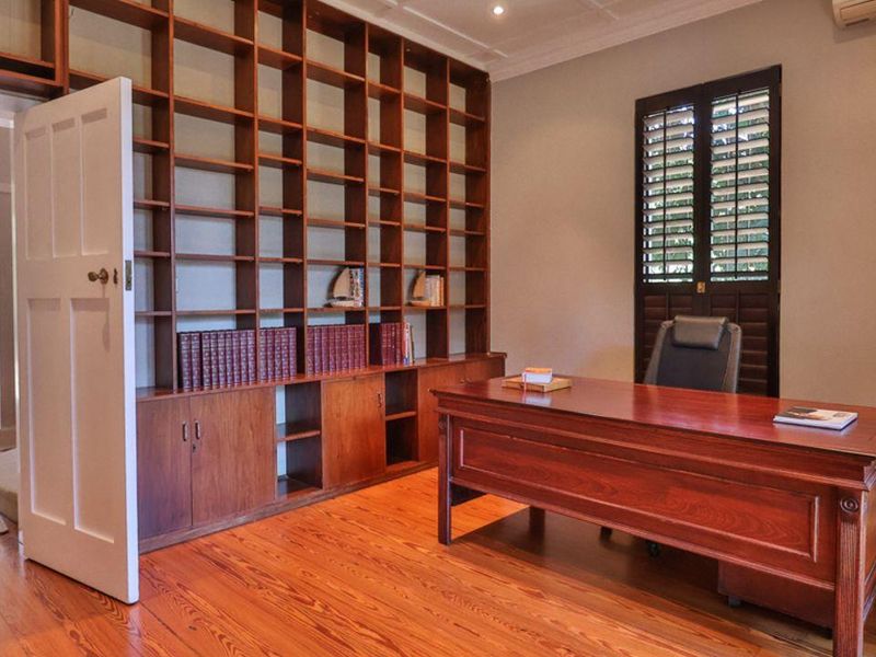 A well-appointed home office featuring extensive built-in timber shelving, polished hardwood flooring, and plantation shutters, offering a sophisticated and functional workspace.