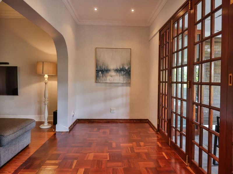 A bright hallway featuring polished parquet flooring, recessed ceiling lighting, and large wooden-framed glass sliding doors leading to an outdoor area.