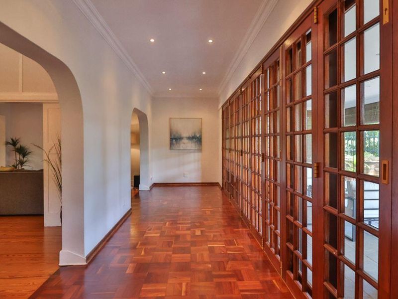 Spacious hallway featuring rich parquet timber flooring, recessed downlighting, and extensive floor-to-ceiling timber-framed glass sliding doors opening to the exterior.