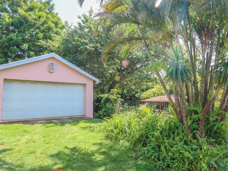 A detached single-car garage with a sectional door, situated in a lush, green garden setting.